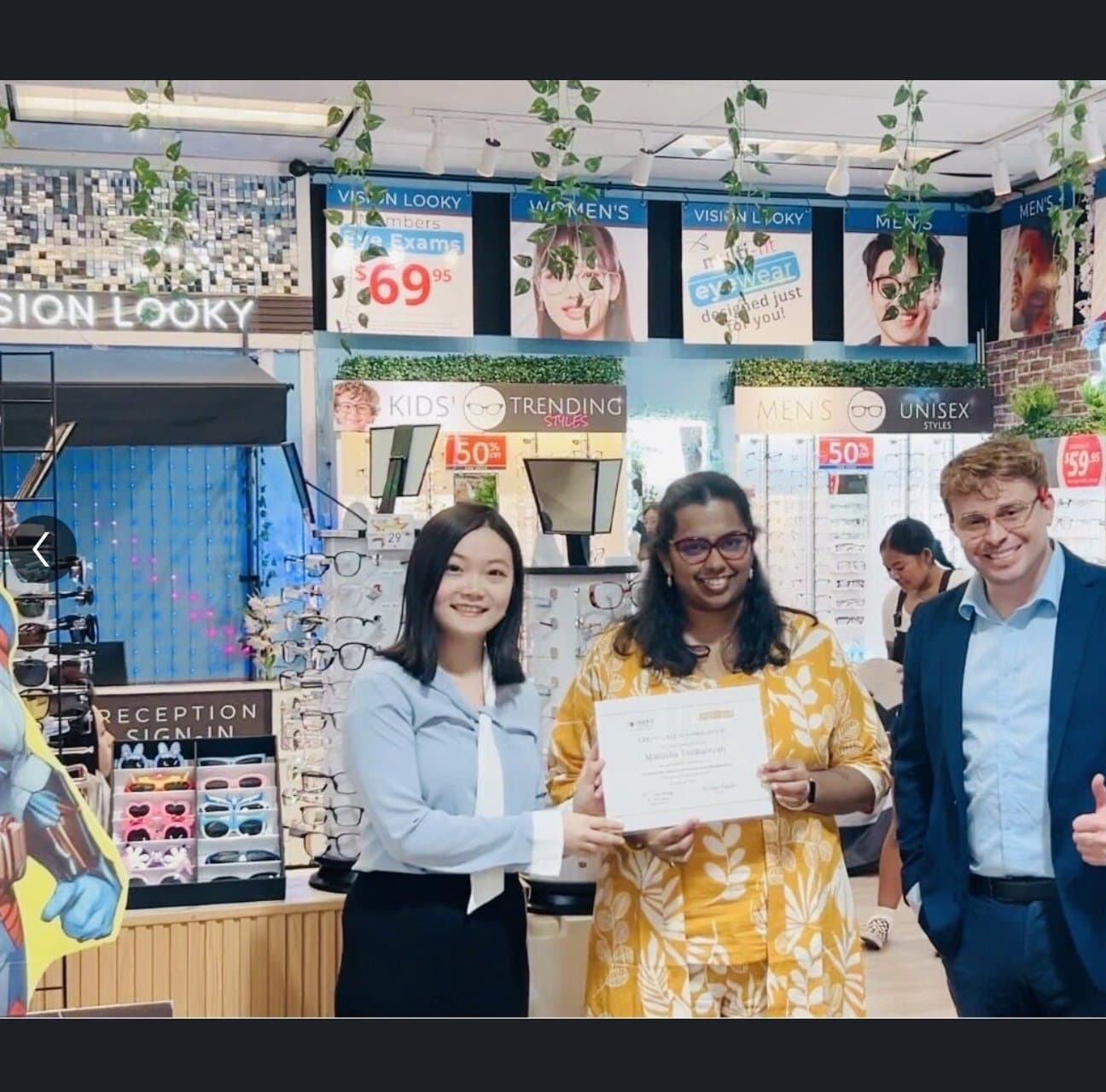 Three interns posing with the Vision Looky Eyeglass-Man superhero standee.